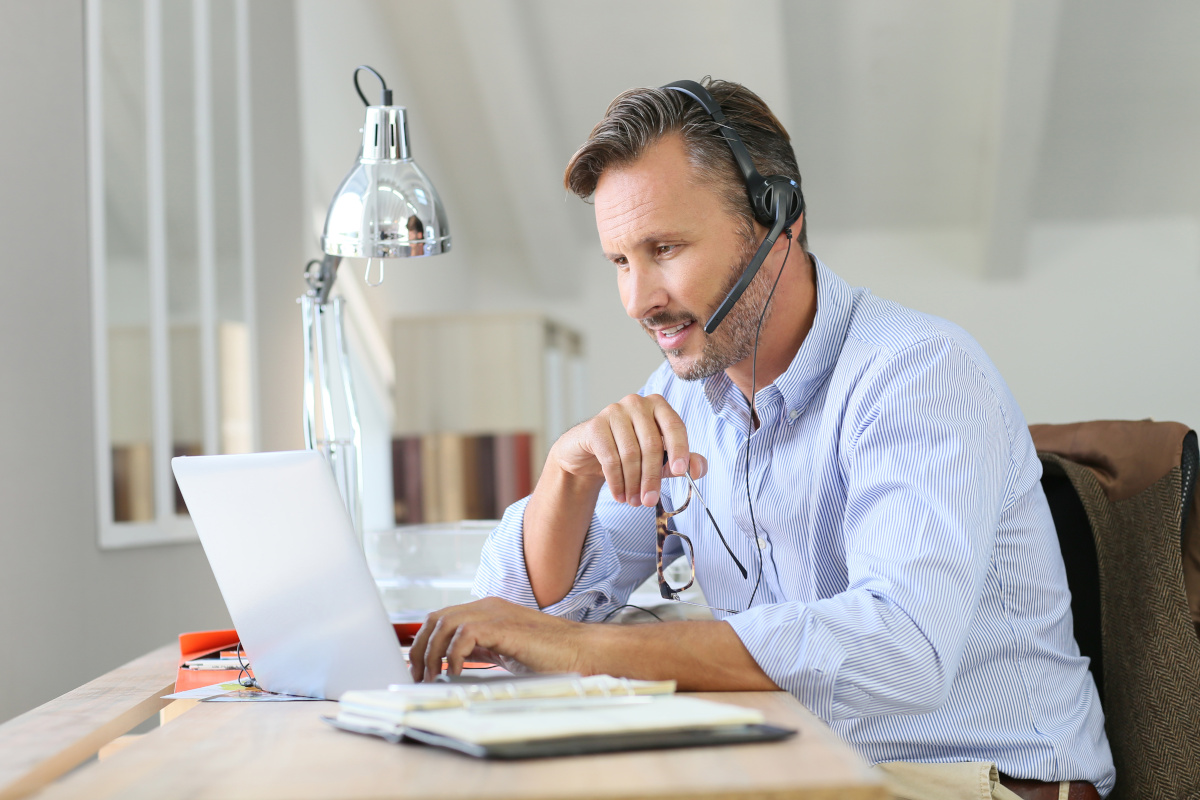 A person with a headset on speaking with a caller while working on a laptop