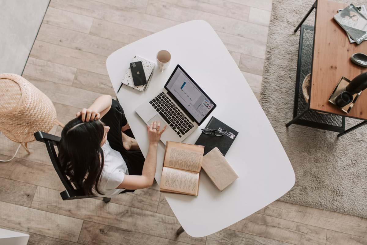 A downward shot of a women working from home on a laptop at a desk in her living room.