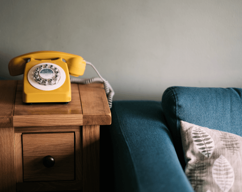 Yellow Rotary Phone on Table Next to Teal Blue Sofa